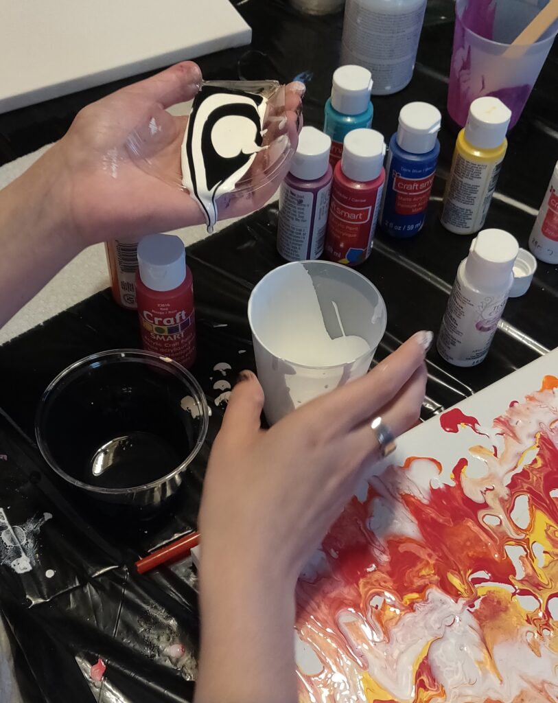 She saw a technique in another video that she is incorporating.   Instead of using a dustpan to layer the black and white paint (like she saw in a different video), she was creative and used a piece of one of the plastic cups.